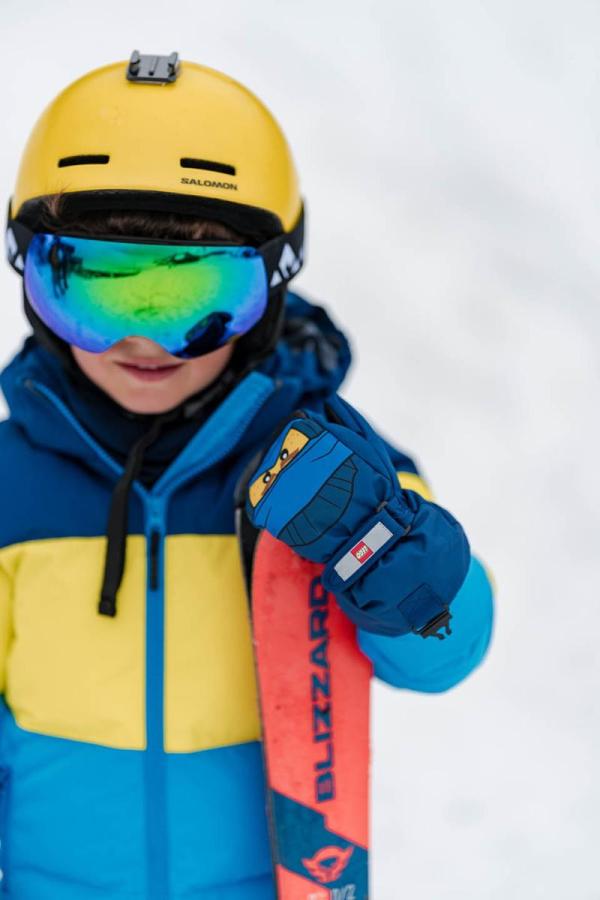 Barn med gul og blå skijakke, hjelm og skibriller.
